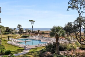 A pool area with lounge chairs and a view of the beach.