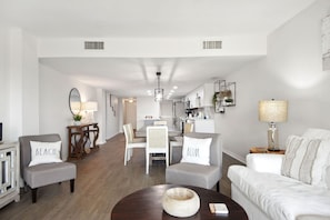 A spacious living room with a dining area, a kitchen, and a hallway leading to another room.