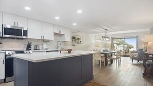 Een moderne keuken met witte kasten, een groot eiland en een eethoek met uitzicht.