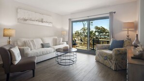 Een moderne woonkamer met een bank, fauteuil en salontafel, een grote schuifdeur die leidt naar een terras met meubels.