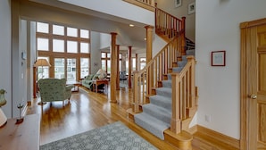 A spacious living room with hardwood floors, a staircase, and large windows allowing natural light. - Doc's Landing: Private Pool, Hot Tub, Currituck Club (Corolla)
