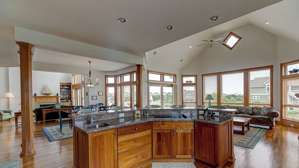 A spacious kitchen with a large island, wooden cabinets, and a view of the backyard through large windows. - Doc's Landing: Private Pool, Hot Tub, Currituck Club (Corolla)