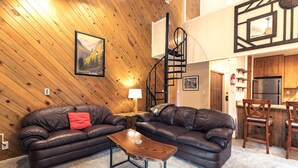 A cozy living room with two leather sofas, a wooden coffee table, and a spiral staircase leading to an upper level. - Motherlode Condo: Walk to Downtown, Slopes (Breckenridge)
