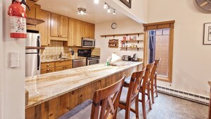 A kitchen with wooden cabinets, a granite countertop, and a built-in microwave. There are bar stools and a fire extinguisher mounted on the wall. - Motherlode Condo: Walk to Downtown, Slopes (Breckenridge)