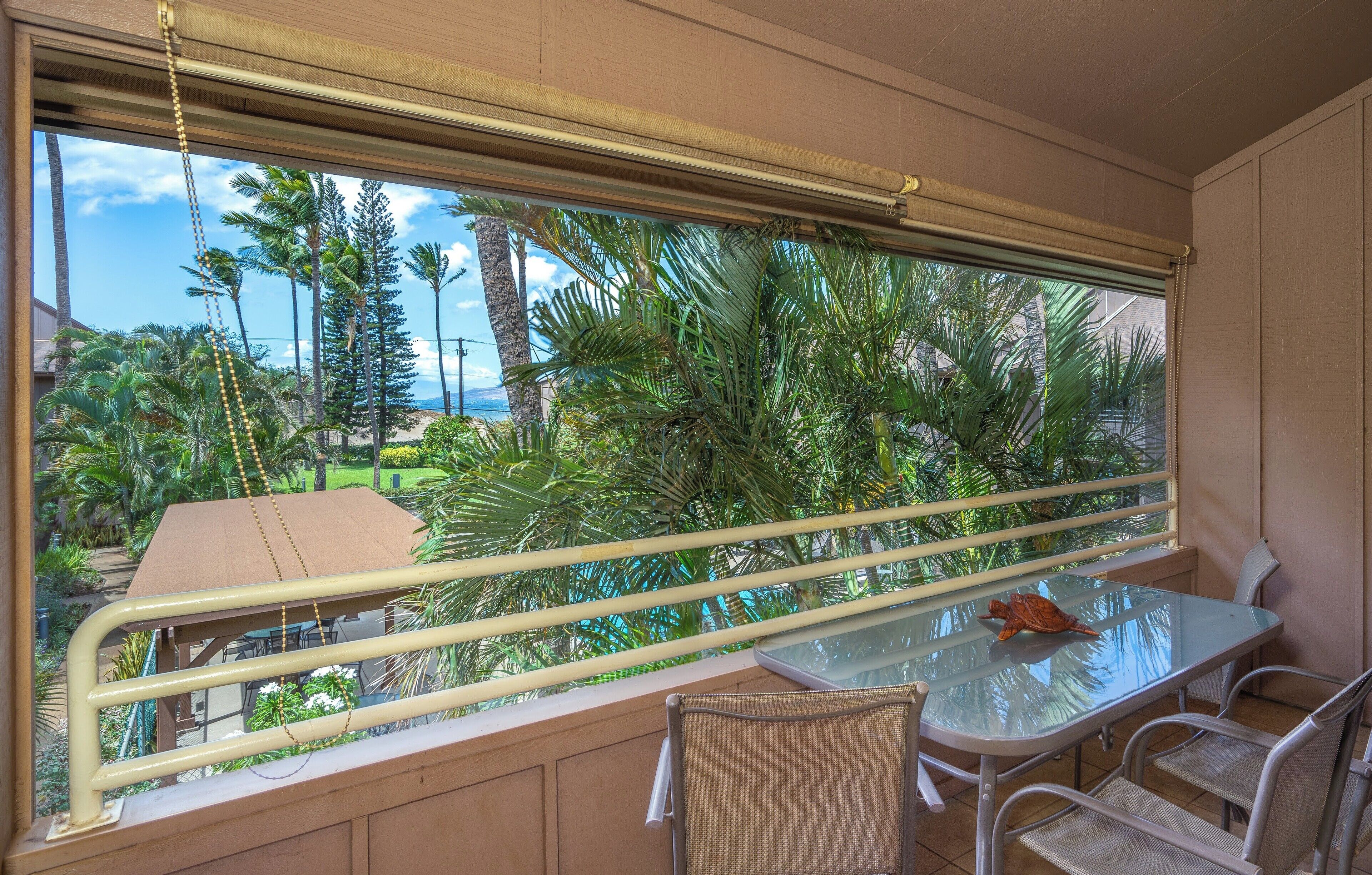 Ein Balkon mit Glastisch und -stühlen, der auf einen tropischen Garten und den Ozean blickt.
