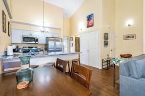 Een moderne keuken met roestvrijstalen apparatuur, een eethoek met een houten tafel en stoelen, en een woonkamer met een bank en een salontafel.