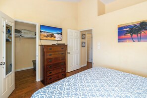 A bedroom with a bed, a dresser, a TV, and a door leading to another room.