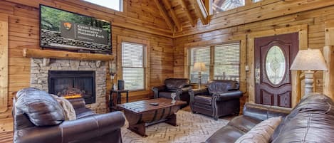 A log cabin interior with a stone fireplace, leather furniture, and a sign for Great Smoky Mountains National Park.