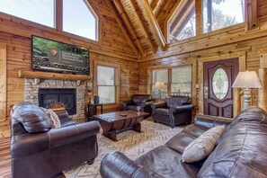 A log cabin interior with a stone fireplace, leather furniture, and a sign for Great Smoky Mountains National Park.