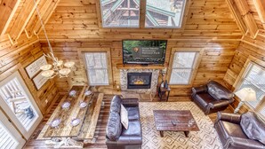 A cozy log cabin interior with a fireplace, leather sofas, a dining table, and a large window overlooking the mountains. - Cabin w/Great Mountain Views-Theater-Arcade-Hot Tub (PIGEON FORGE)