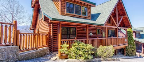A log cabin with a prominent front porch, a second-story balcony, and a stone foundation.
