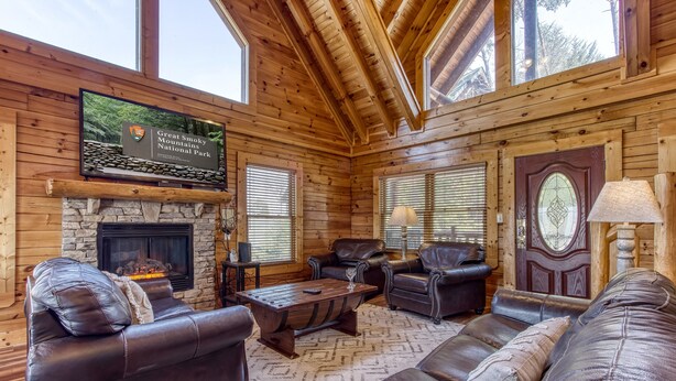 A log cabin interior with a stone fireplace, leather furniture, and a sign for Great Smoky Mountains National Park. - Cabin w/Great Mountain Views-Theater-Arcade-Hot Tub (PIGEON FORGE)