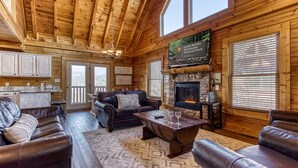 A wooden cabin interior with a fireplace, leather sofas, and a stone fireplace surround. - Cabin w/Great Mountain Views-Theater-Arcade-Hot Tub (PIGEON FORGE)