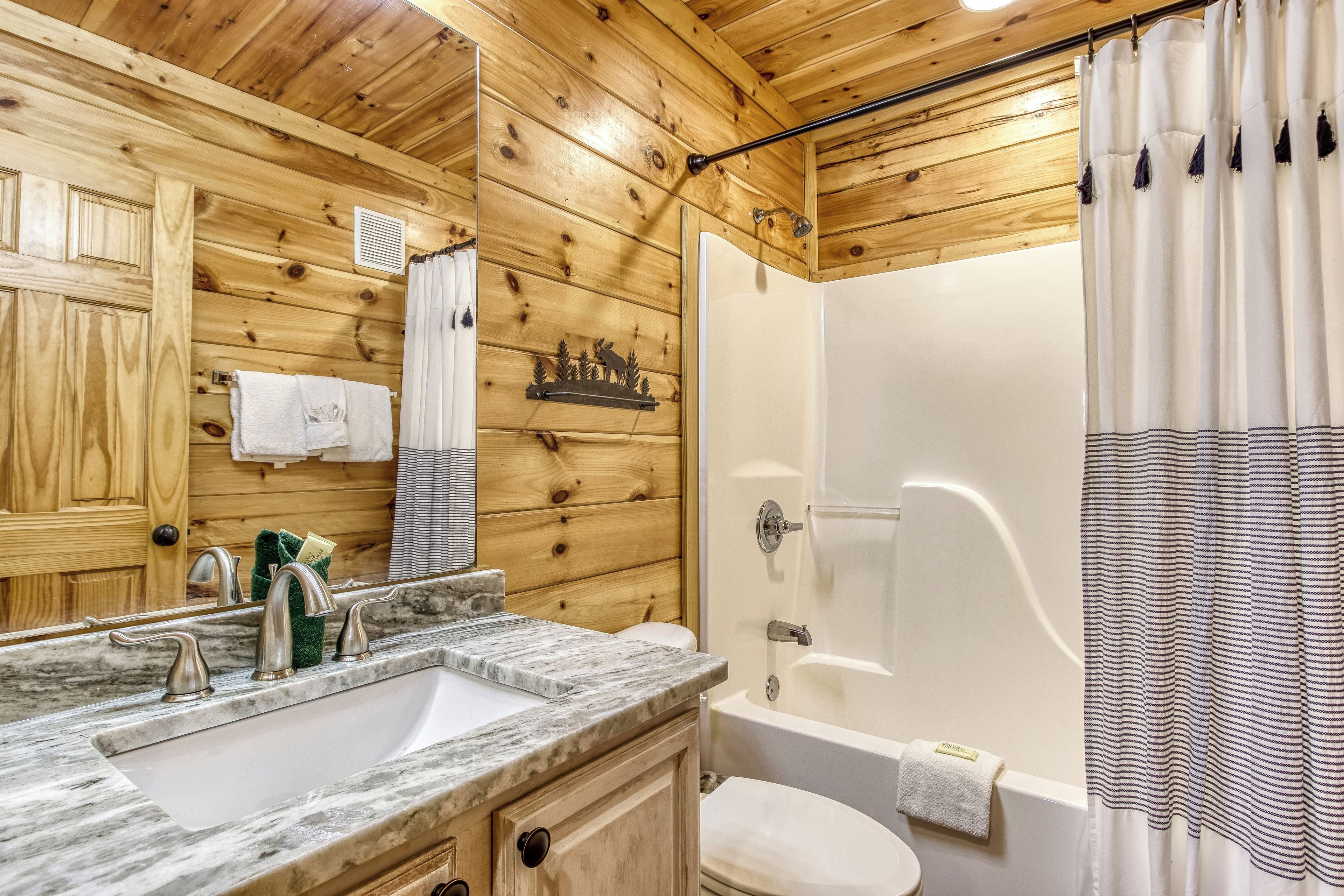 A wooden cabin bathroom with a sink, mirror, toilet, and shower.