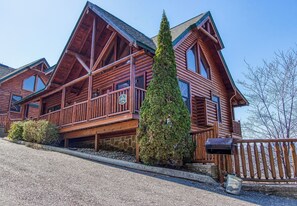 A large, multi-story log cabin with a prominent front porch and a steeply pitched roof.