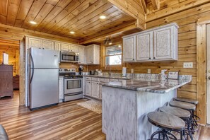 Una cocina con armarios de madera, un refrigerador de acero inoxidable, un horno, un microondas y una encimera de mármol.