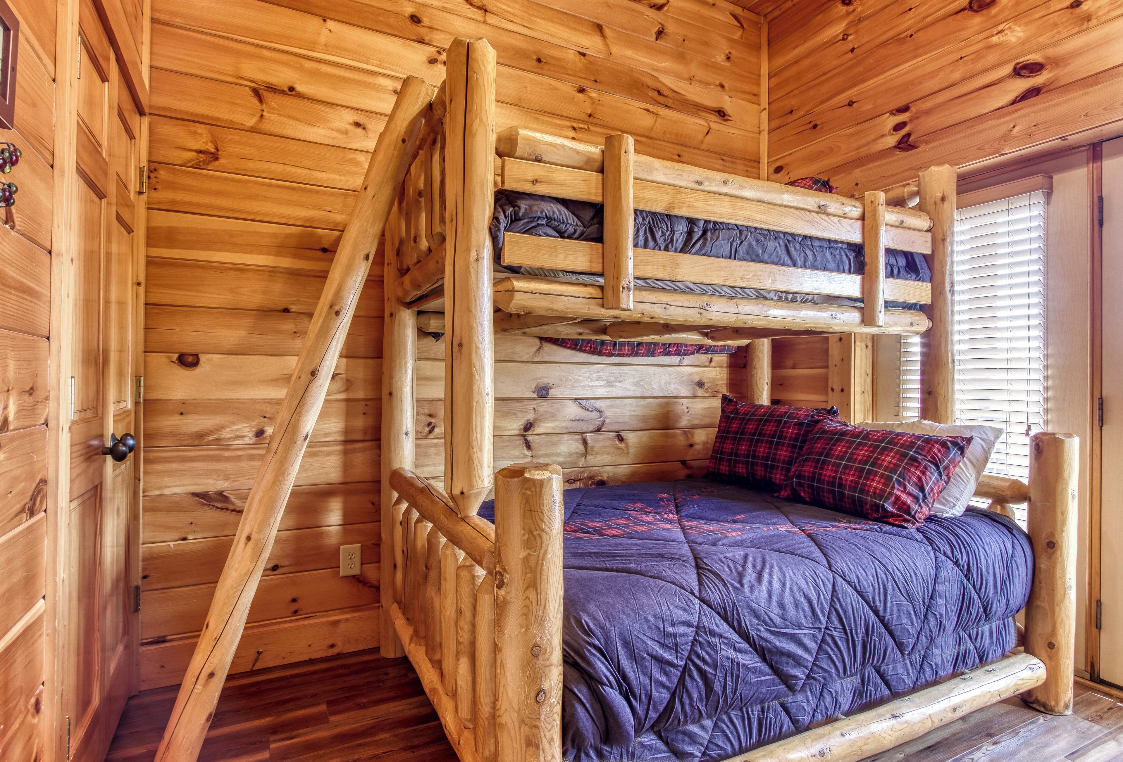 A wooden bunk bed with a blue quilted mattress and plaid pillow.
