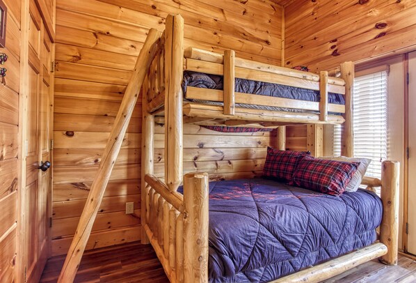 A wooden bunk bed with a blue quilted mattress and plaid pillow.