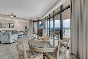 A spacious living area with a glass-top dining table, comfortable seating, a television, and a balcony with a view. - The Oasis At Orange Beach 501 by Liquid Life (Orange Beach)