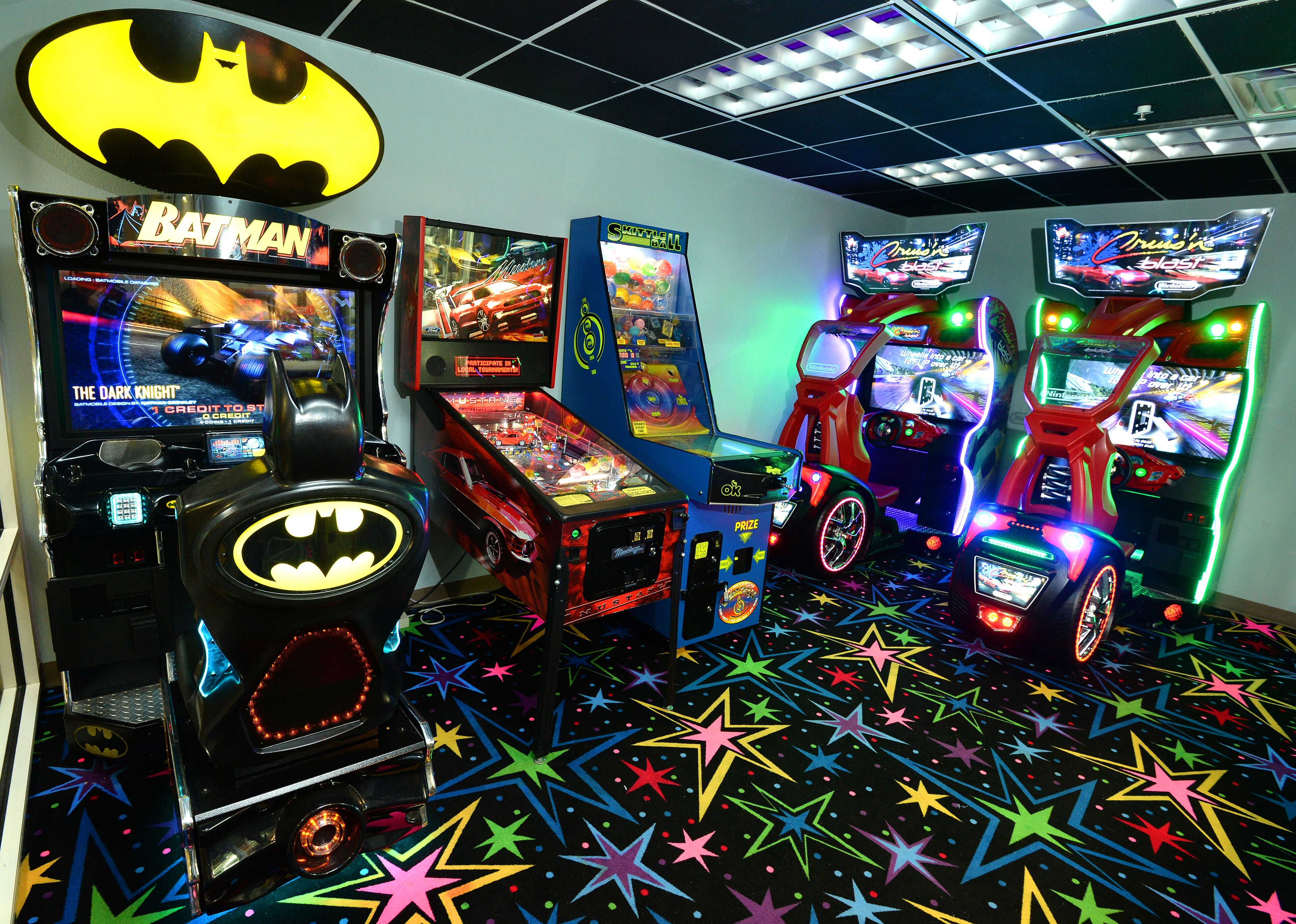 Ein Raum mit Spielhallenspielen, darunter Batman und Rennspiele, sowie einem fußbodenförmigen Sternenmuster.
