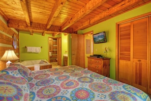 A bedroom with a wooden ceiling, a bed with a colorful patterned bedspread, a dresser, a television on the wall, and a door leading to another room. - Gatlinburg | Arcade | Hot Tub | Fireplace | WiFi (Gatlinburg)