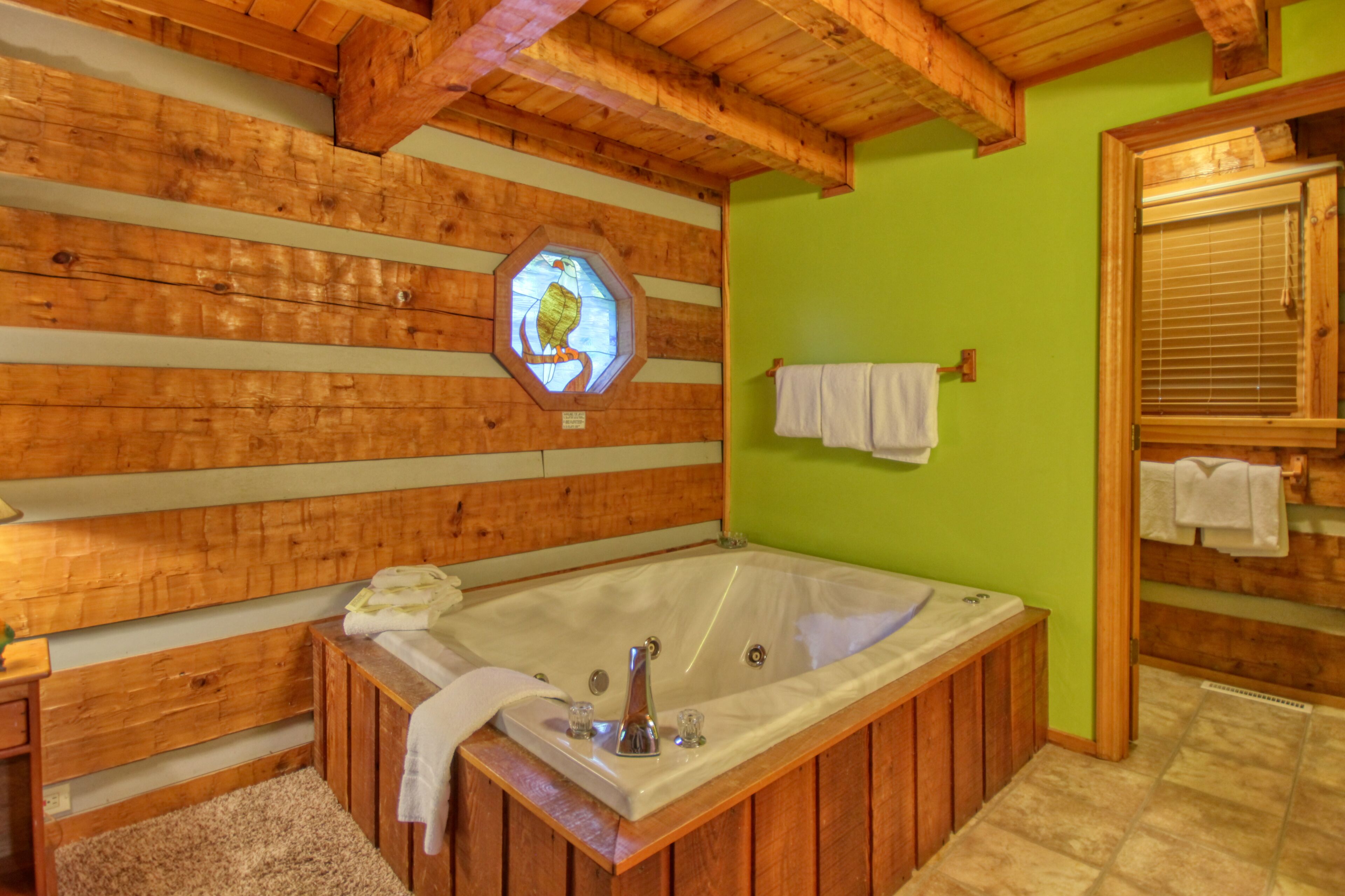 Une salle de bain de style cabane en bois, dotée d’une grande baignoire, de poutres en bois et d’un mur vert.