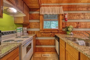 A compact kitchen with wooden walls, a window with a view, a sink, and a stove. - Gatlinburg | Arcade | Hot Tub | Fireplace | WiFi (Gatlinburg)