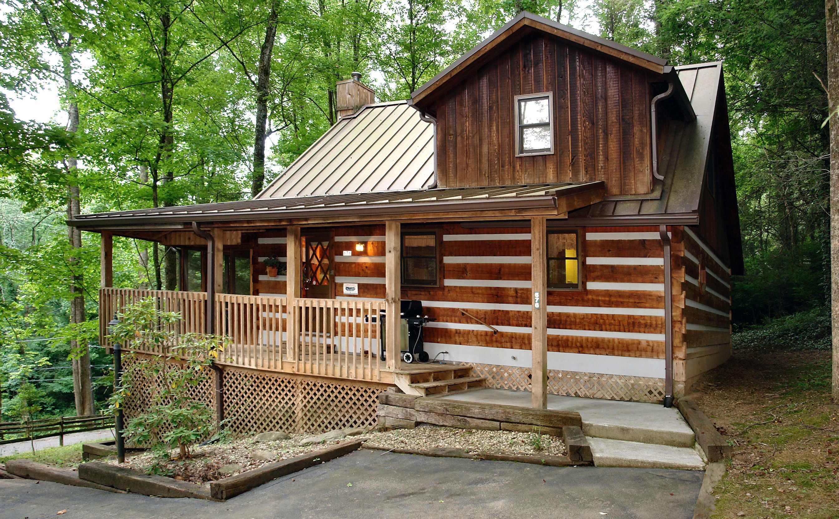 A rustic log cabin with a wooden porch, a metal roof, and a small deck area.
