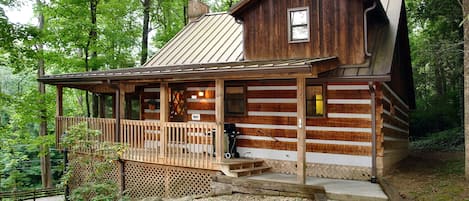 A rustic log cabin with a wooden porch, a metal roof, and a small deck area.