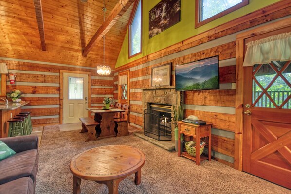 A log cabin interior with a fireplace, wooden walls, a dining area, and a cozy seating space.