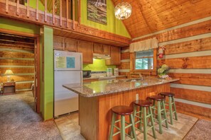 A rustic kitchen with wooden walls, a granite countertop, and a refrigerator.