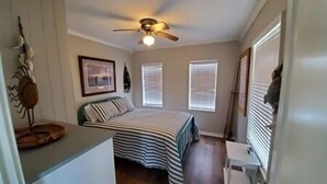 A bedroom with a bed, a ceiling fan, a window with blinds, and a small table. - Laguna Flats Lodge. 3 Bedroom, 2 Bath. Close to Public Pier or Boat Launch. (Port Mansfield)