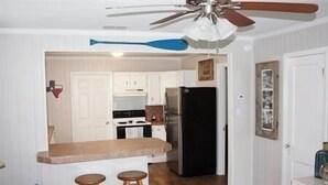 A kitchen with white cabinets, a black refrigerator, and a wooden countertop. There are two wooden stools and a ceiling fan. - Laguna Flats Lodge. 3 Bedroom, 2 Bath. Close to Public Pier or Boat Launch. (Port Mansfield)
