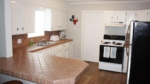 A kitchen with white cabinets, a tiled island, a stove, and a refrigerator. - Laguna Flats Lodge. 3 Bedroom, 2 Bath. Close to Public Pier or Boat Launch. (Port Mansfield)