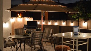An outdoor patio with a table and chairs, a grill, and string lights.