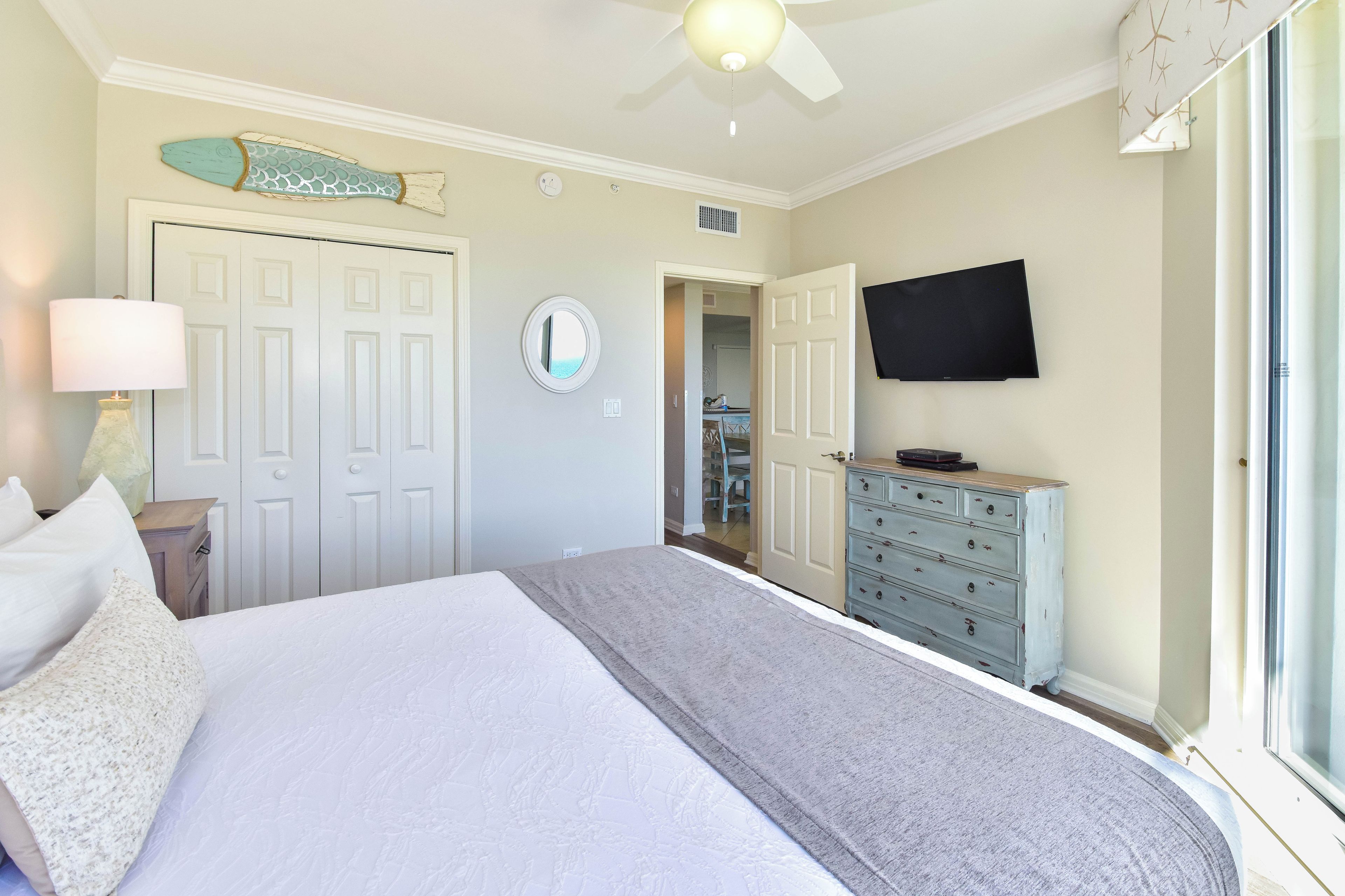 A bedroom with a bed, dresser, TV, and a ceiling fan.
