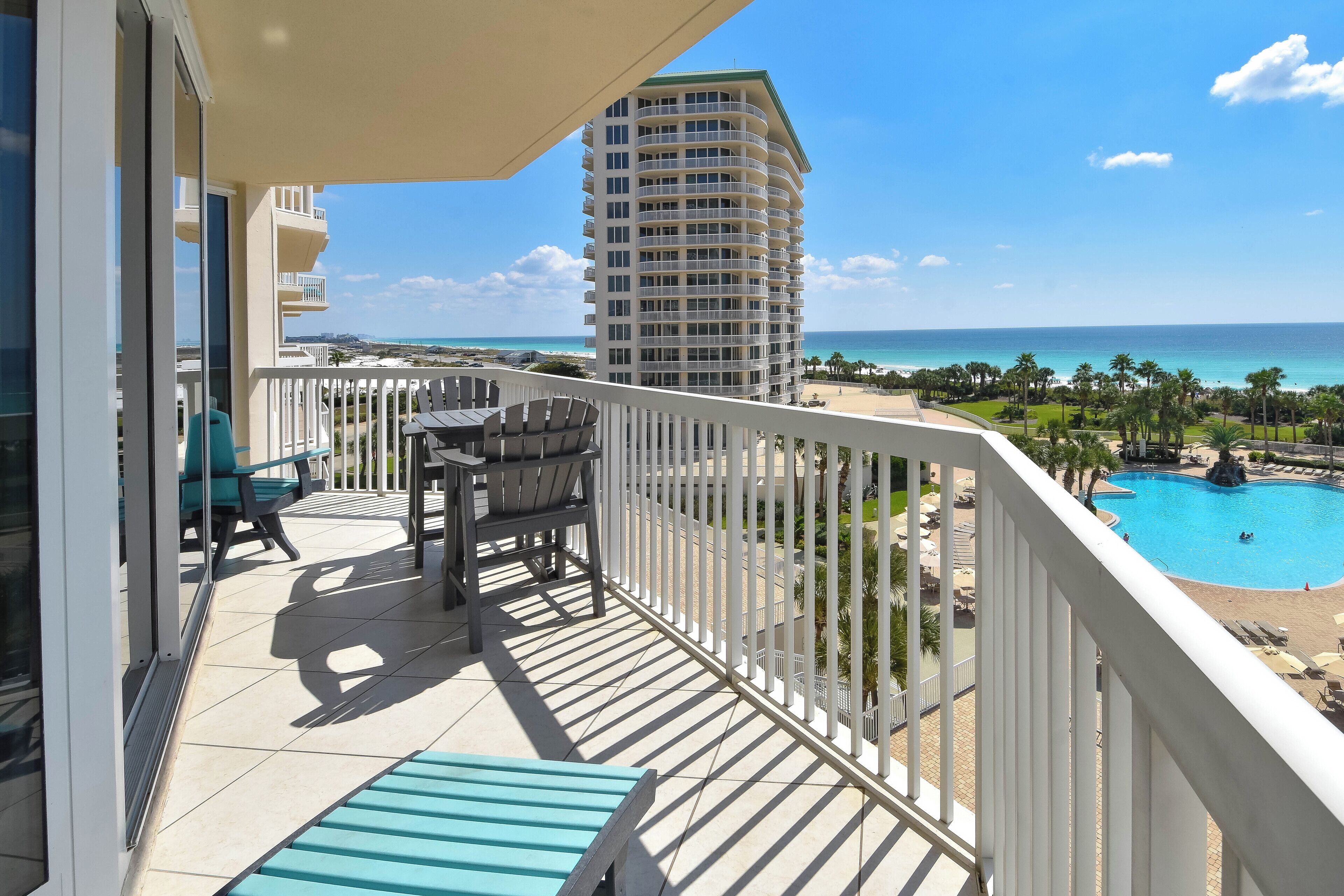 A balcony with a view of a beach, a pool, and a tall building.
