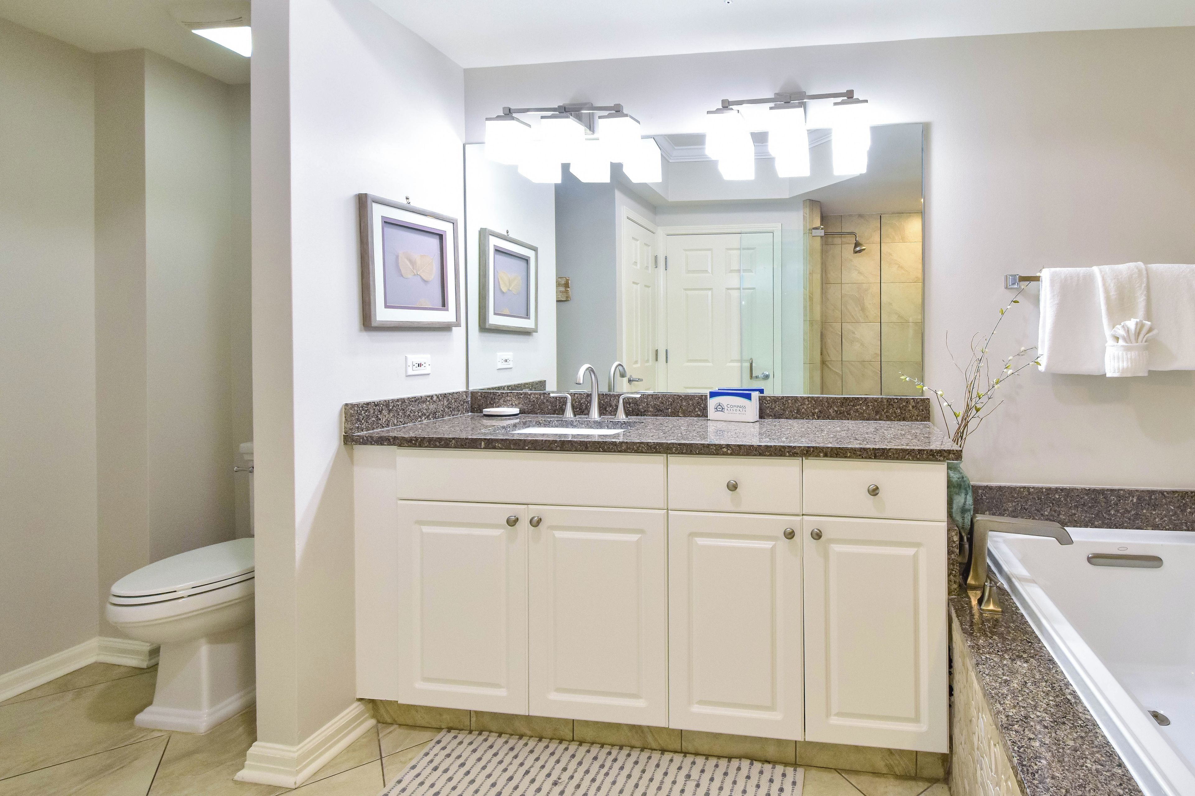 A bathroom with a white vanity, a sink, a mirror, and a shower area.