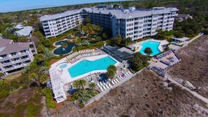 A resort with multiple swimming pools, a large building with balconies, and a landscaped area with palm trees.