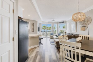 Eine moderne Küche mit einem schwarzen Kühlschrank, eine Essecke mit einem Holztisch und -stühlen und Blick auf den Strand durch große Fenster.