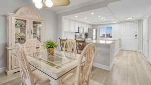 Una cocina moderna con armarios blancos, una mesa de comedor de vidrio y un ventilador de techo.