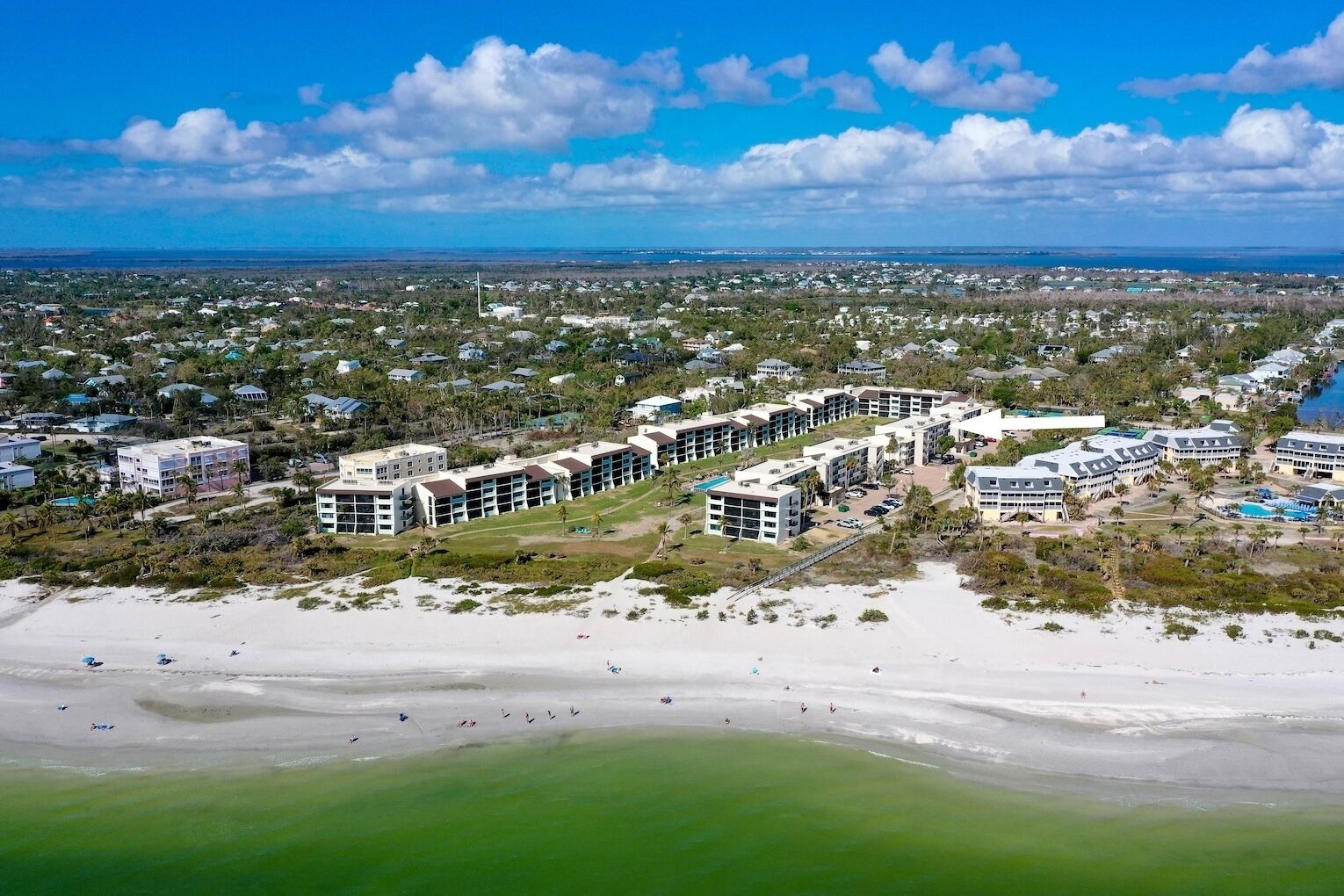 An aerial view of a coastal resort with multiple hotel buildings, a beach, and a clear view of the ocean.