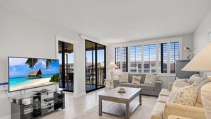 Una sala de estar moderna con un televisor de pantalla plana, un sofá gris, una mesa de centro de madera y un ventanal con vistas a un balcón.