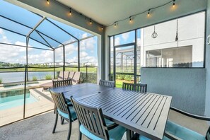 A covered outdoor dining area with a pool, large windows, and hanging lights.