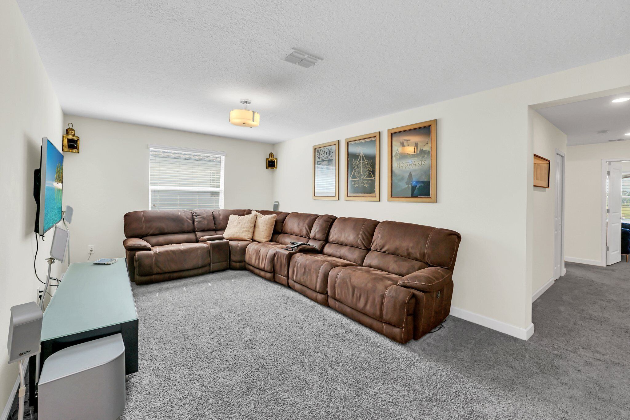 A living room with a brown leather sectional sofa, a small table, and a TV. There are three framed pictures on the wall.