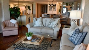 A living room with a beige sofa, a glass coffee table with a woven basket, a small armchair, and a lamp. - Ocean One 413 - Oceanfront 4th Floor Condo (Hilton Head Island)