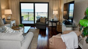 A living room with a sofa, armchair, and a television. There is a balcony with a view of the ocean. - Ocean One 413 - Oceanfront 4th Floor Condo (Hilton Head Island)