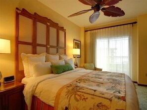 Relax in this inviting room with a large bed and ceiling fan, surrounded by sheer curtains.