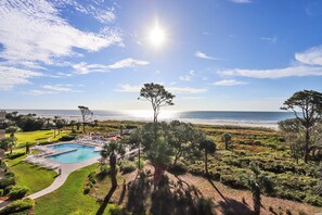 Relax by the serene pool surrounded by lush greenery and mature trees, overlooking a pristine beach.