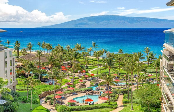 A resort with a pool area, palm trees, and a view of the ocean. - Maui Resort Rentals: Honua Kai Konea 831 - Stunning 8th Floor Ocean View Studio (Lahaina)